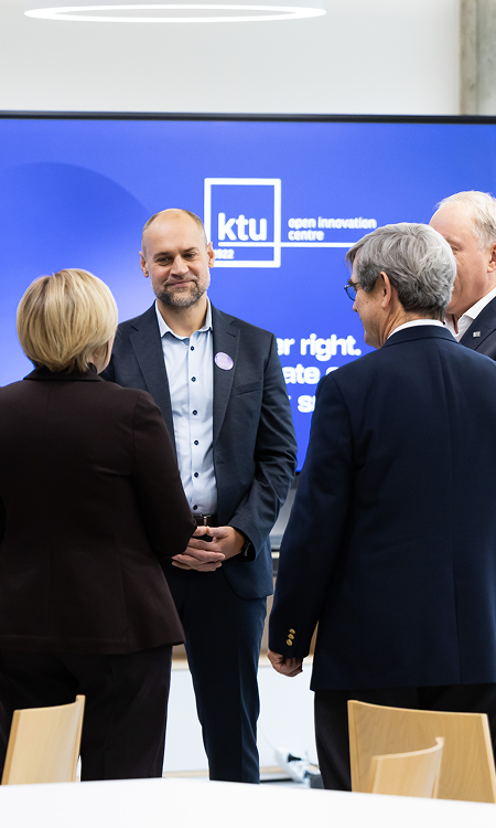 Profesionalų grupė stovi ir bendrauja prie&scaron;ais ekraną, kuriame matoma KTU Atvirųjų inovacijų centro simbolika.